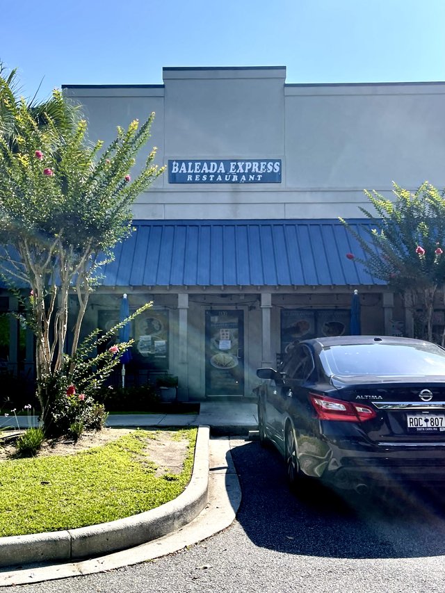 Baleada Express Restaurant storefront with blue metal awning and crepe myrtles, Bluffton SC