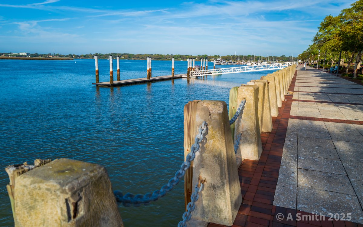 Chains and docks. The promenade railing up close, the marina docks spread out beyond.