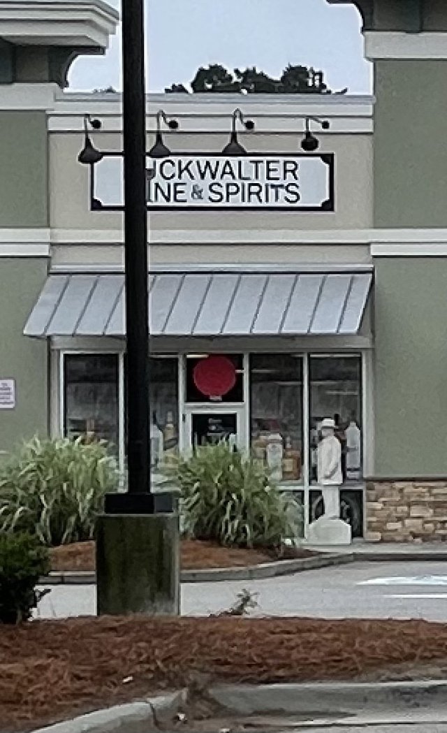 Buckwalter Wine & Spirits sign partly behind a light pole, statue in the window, Bluffton SC