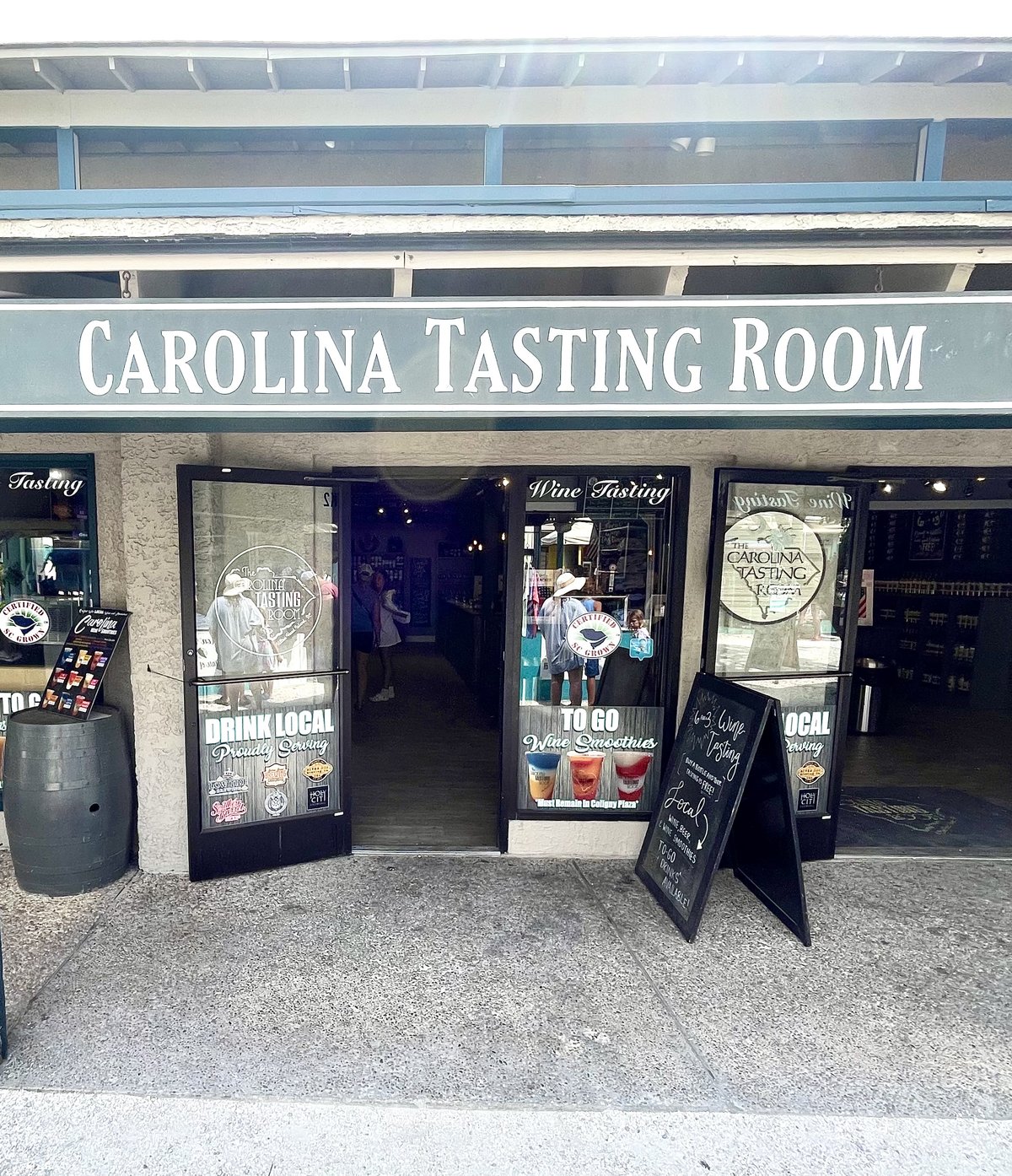 Carolina Tasting Room at Coligny — the big serif sign over open glass doors, DRINK LOCAL on one door and wine smoothies on the other