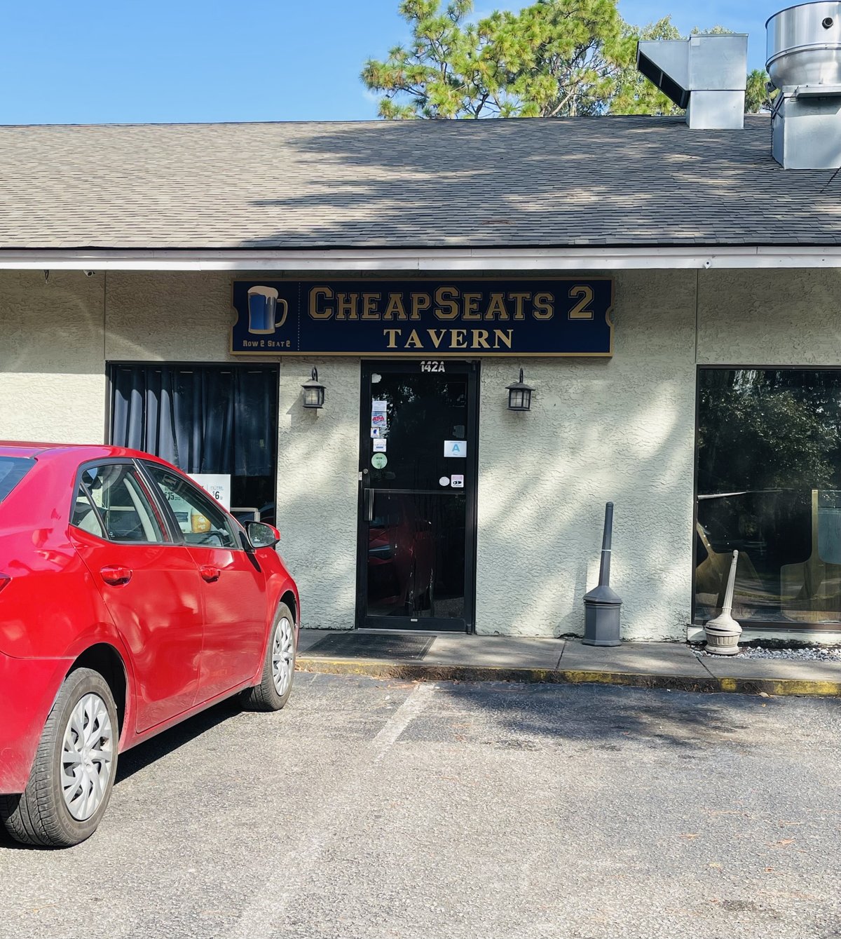 Cheap Seats 2 Tavern storefront in Bluffton — the navy sign with a beer mug over door 142A, red car parked in front