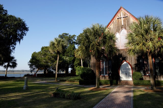 The Church of the Cross in Bluffton — weathered wooden church with palmettos, a brick path and the May River behind