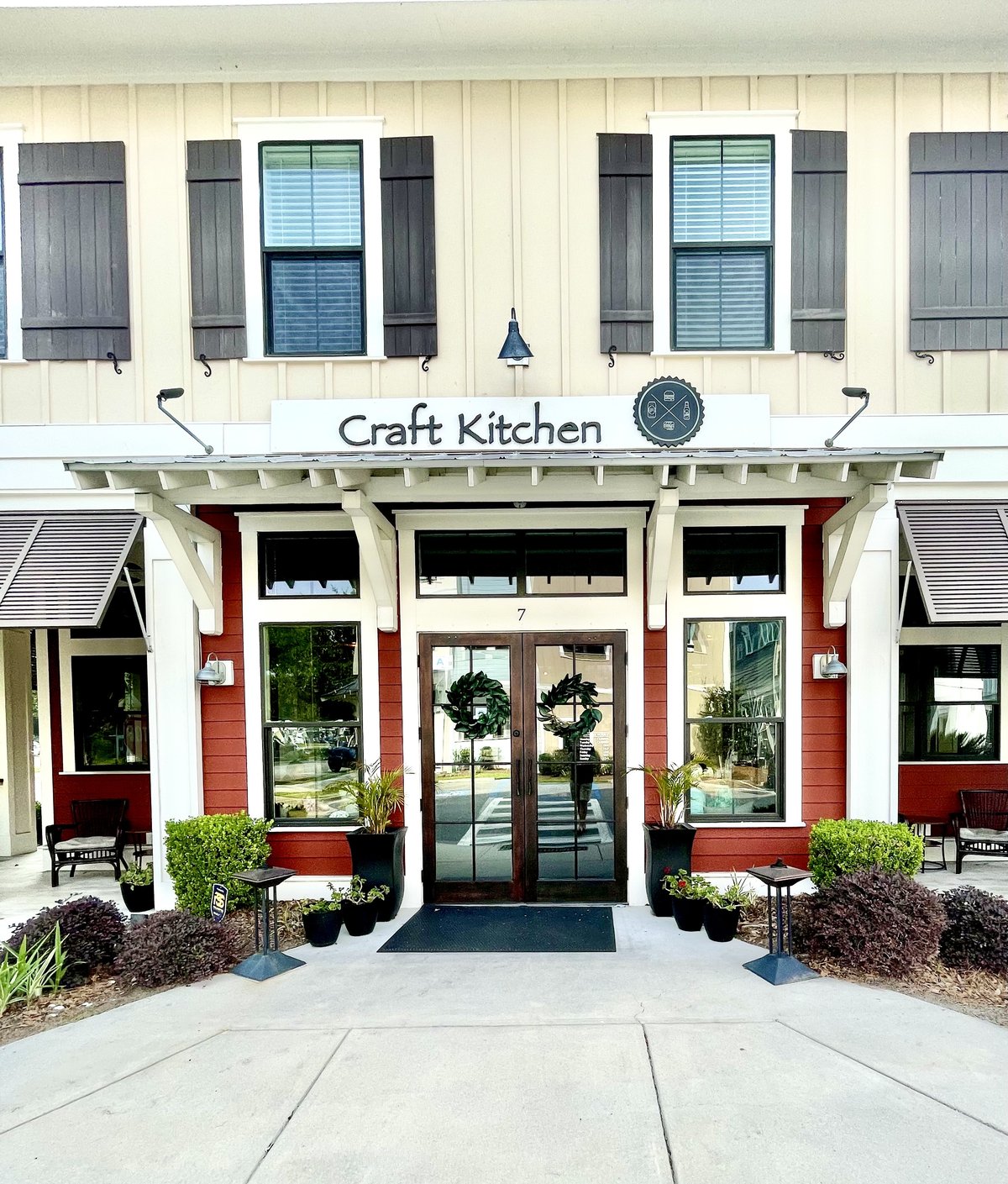 Craft Kitchen from the sidewalk — board-and-batten siding, wreaths on the double doors and the bottle-cap logo over the porch