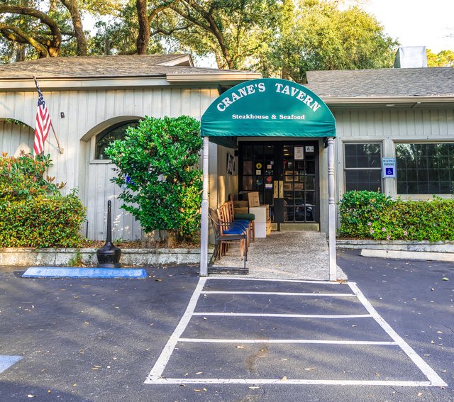 Crane's Tavern on Hilton Head Island — the green arched awning over the entrance, benches under it and a flag by the door