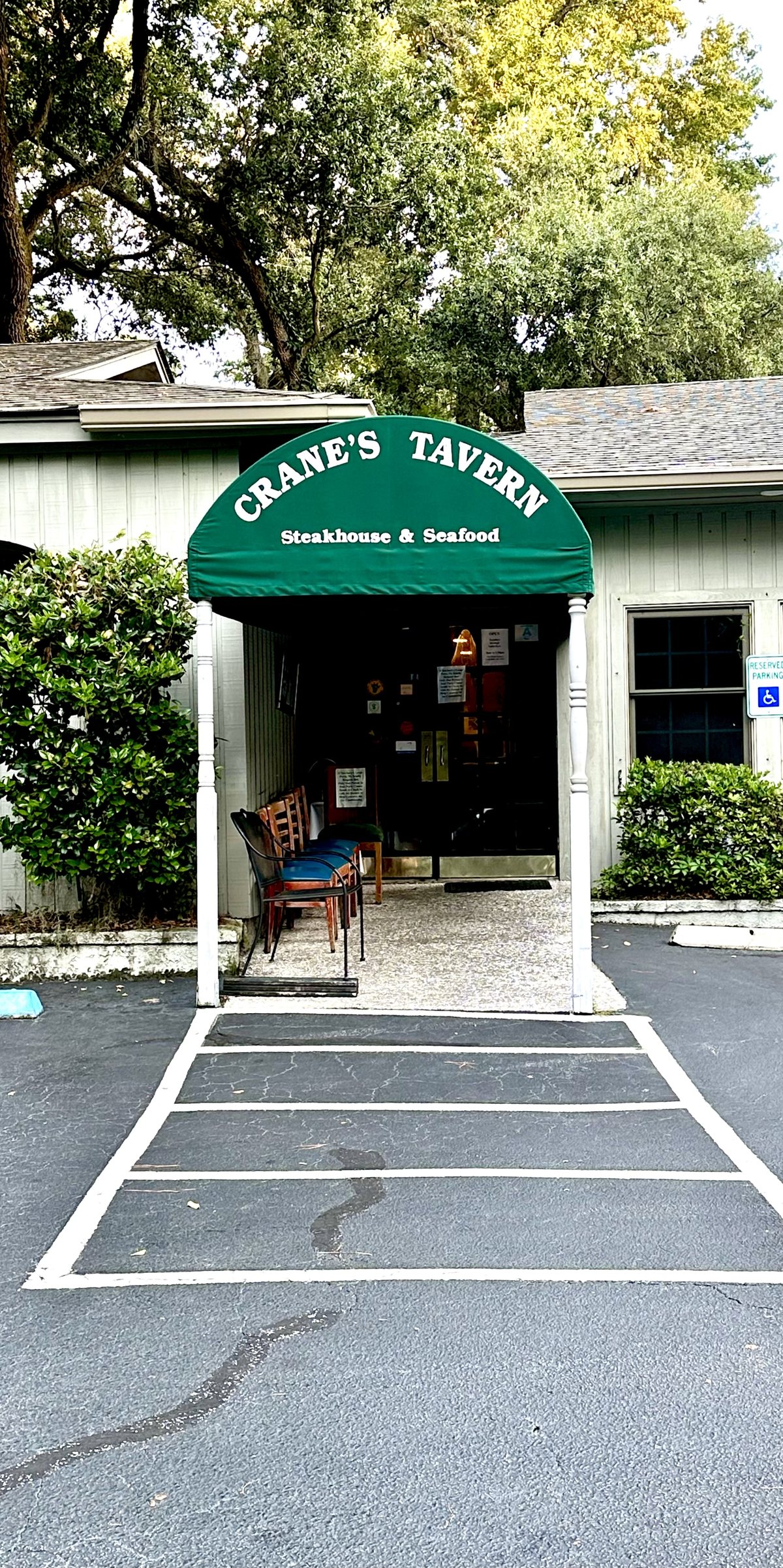 Crane's Tavern entrance up close — the green arched awning reading Steakhouse and Seafood, chairs set out by the door