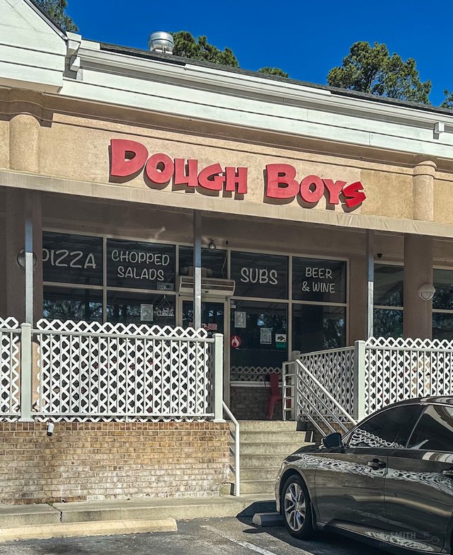 Dough Boys restaurant front on Hilton Head Island — red bubble letters, windows lettered Pizza, Chopped Salads, Subs, Beer and Wine, white lattice patio fence