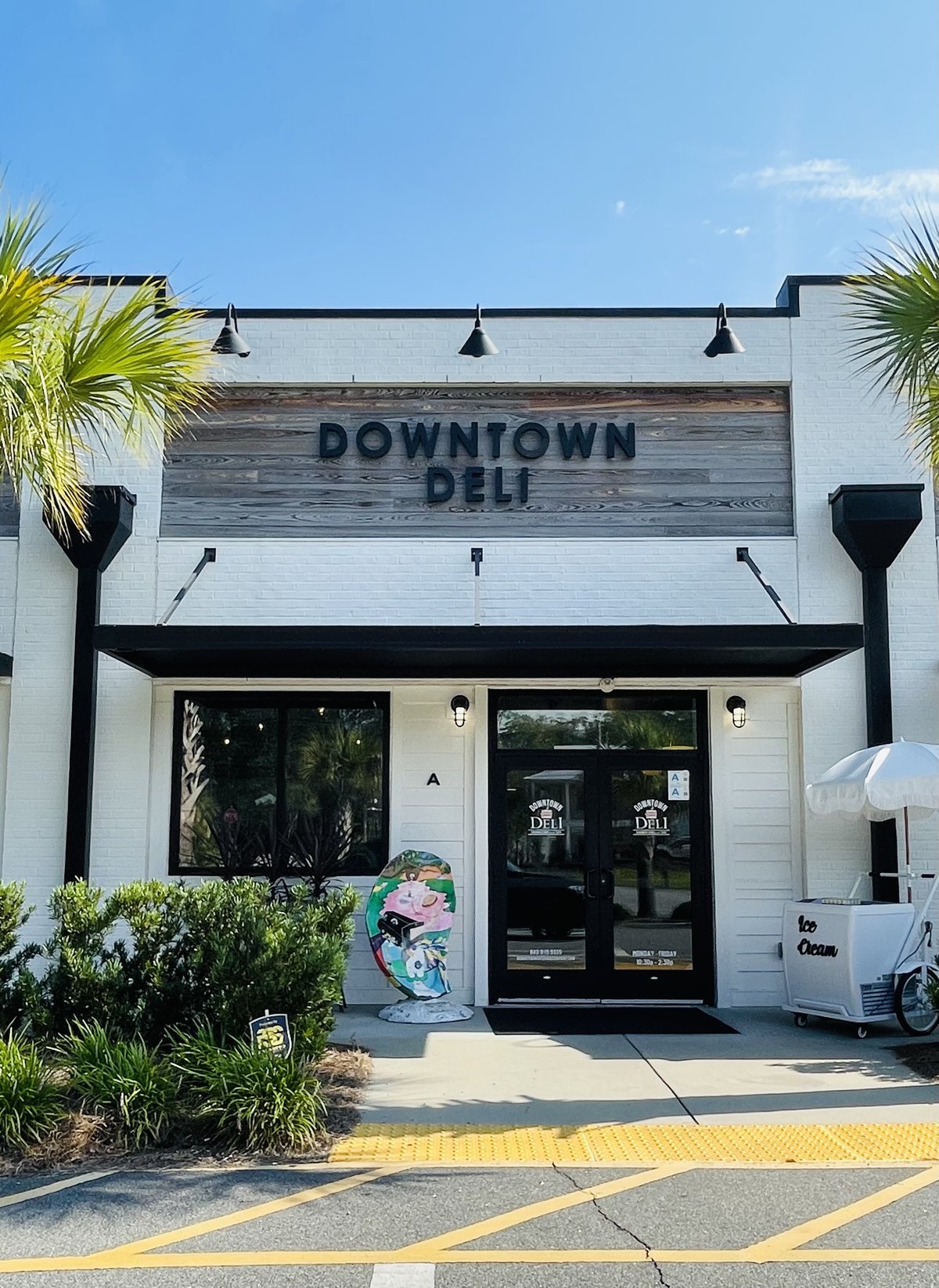Downtown Deli storefront in Bluffton — white brick, a weathered-wood sign, and a painted oyster by the door