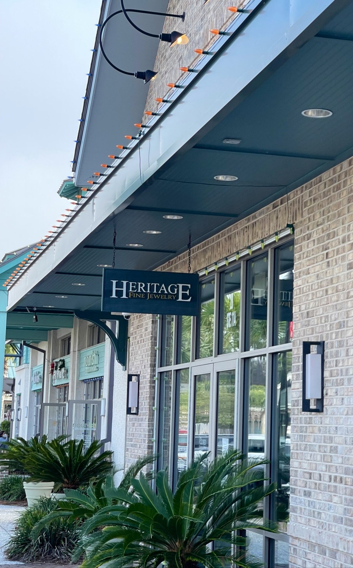 Heritage Fine Jewelry at Shelter Cove, Hilton Head Island — the hanging sign under the covered walkway, sago palms by the glass front
