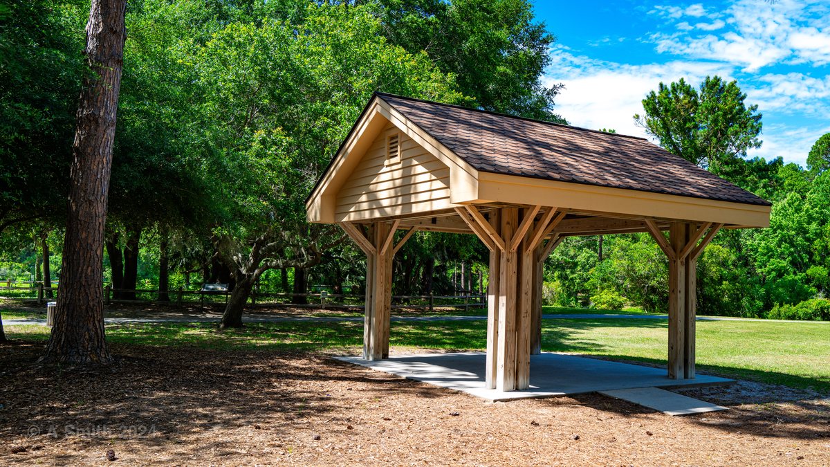 The small shelter. A gabled picnic shelter in the pines off the lawn.