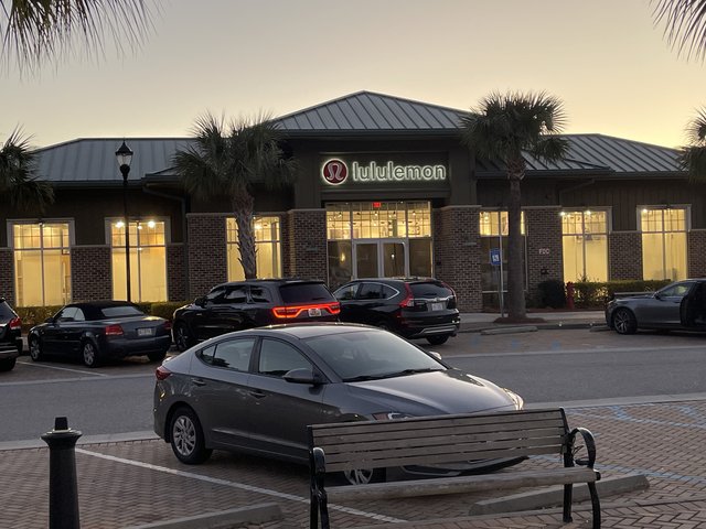lululemon at Shelter Cove on Hilton Head Island at dusk — the lit red logo, brick front, palmettos and cars heading home