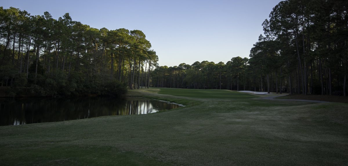 North Course, Hole 15. The 15th fairway bends along the pond in low light.