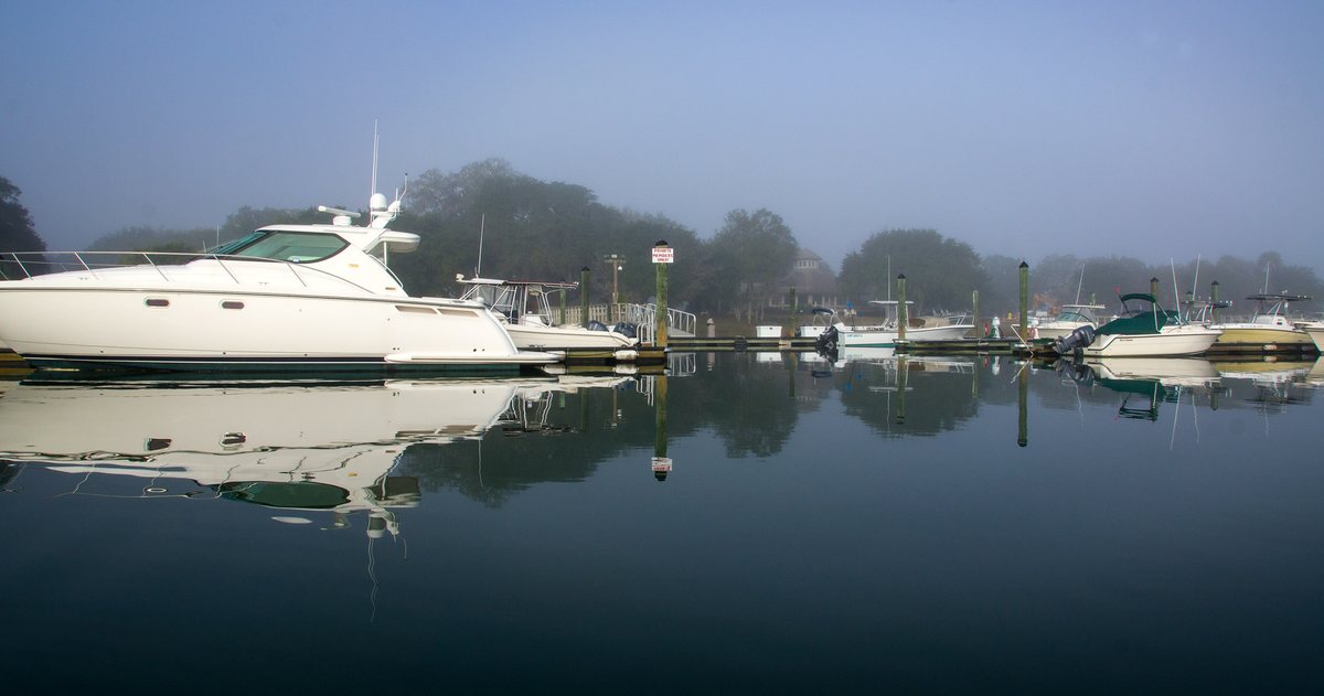 Marina fog. Yachts at their slips, mirrored in still, foggy water.