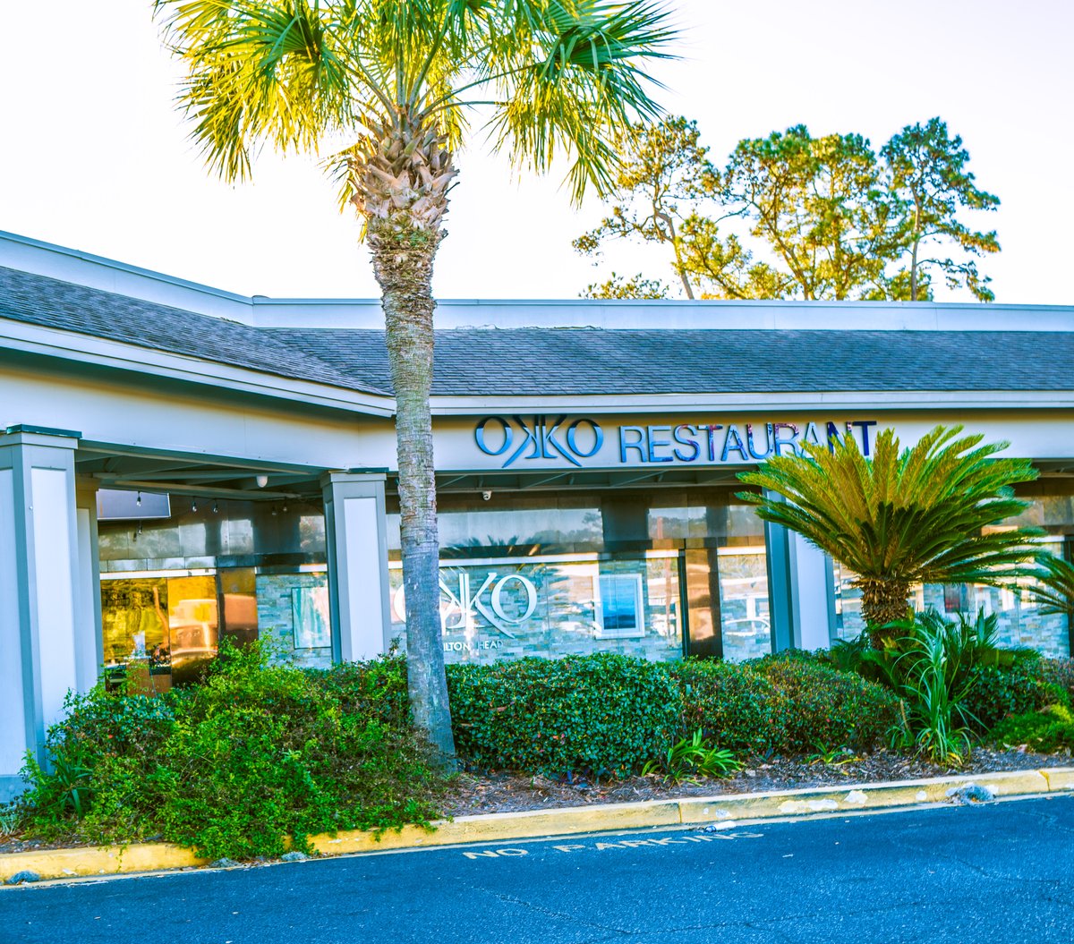 OKKO Restaurant on Hilton Head Island — blue letters over a glass front, a palmetto and a sago palm framing the entrance