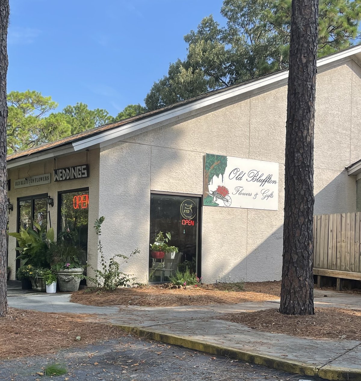 Old Bluffton Flowers & Gifts storefront in Bluffton — the script sign with a flower cart, WEDDINGS over the door, plants out front