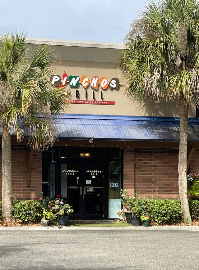 Pinchos Grill at Tanger Outlets 1 in Bluffton — the colorful letter sign, blue metal awning and two palmettos framing the door