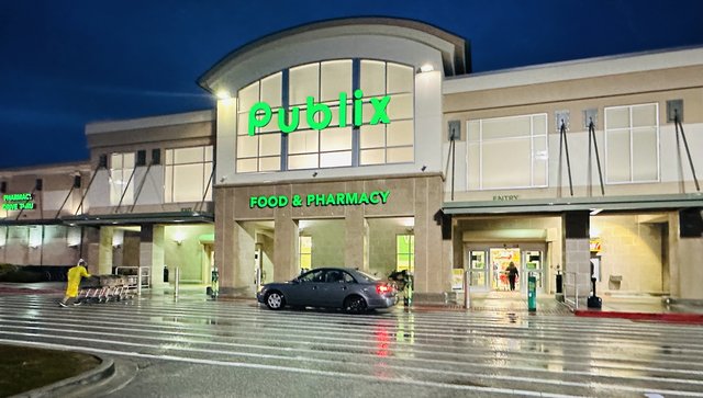 Publix in Hardeeville at night in the rain — green letters and FOOD & PHARMACY lit over the entry, reflections on the wet lot