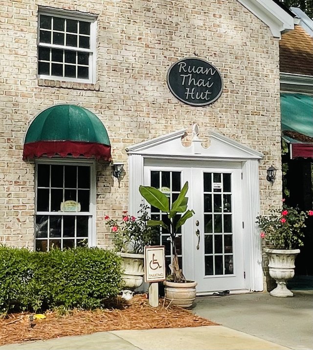 Ruan Thai Hut in Main Street Village — the oval sign on the brick wall, green-and-red dome awning and white French doors