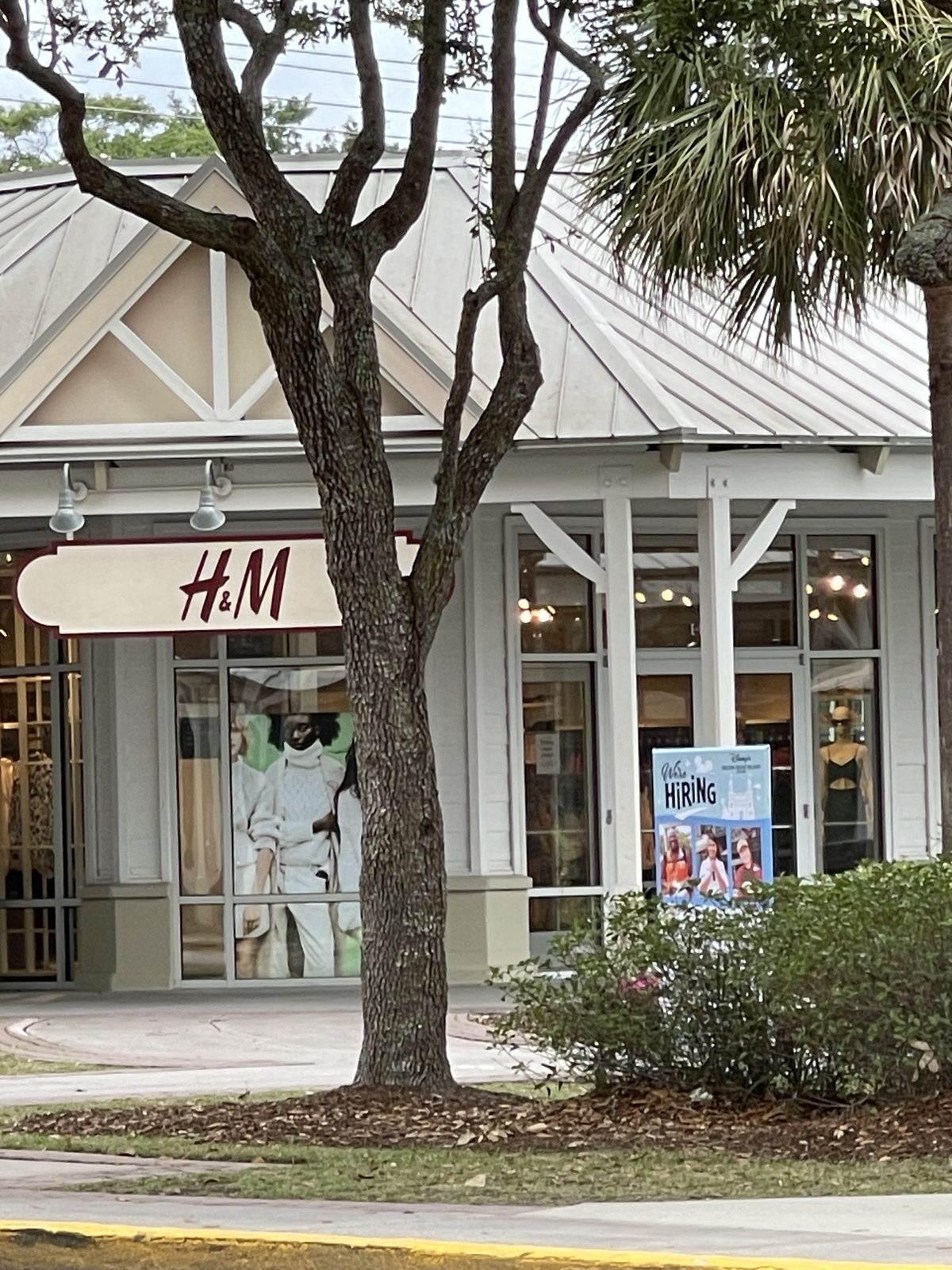 H&M at Tanger Outlets 2 — red letters on a white blade sign behind an oak tree