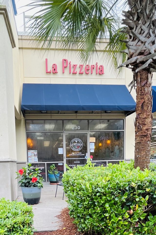 La Pizzeria at Tanger Outlets 2 — pink letters over a navy awning, a palm leaning into frame