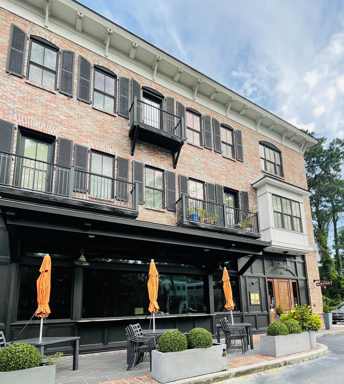 The Promenade Building in Old Town Bluffton — three stories of brick with black shutters and balconies over a ground-floor patio