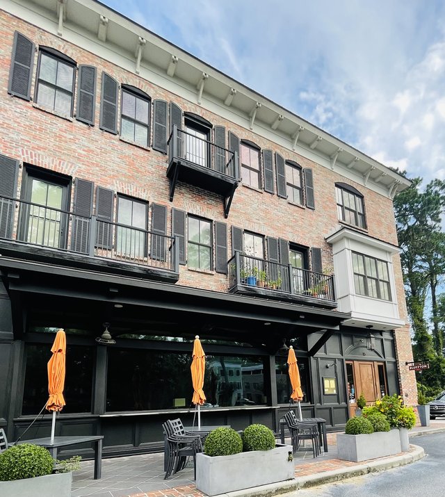 The Promenade Building in Old Town Bluffton — three stories of brick with black shutters and balconies over a ground-floor patio