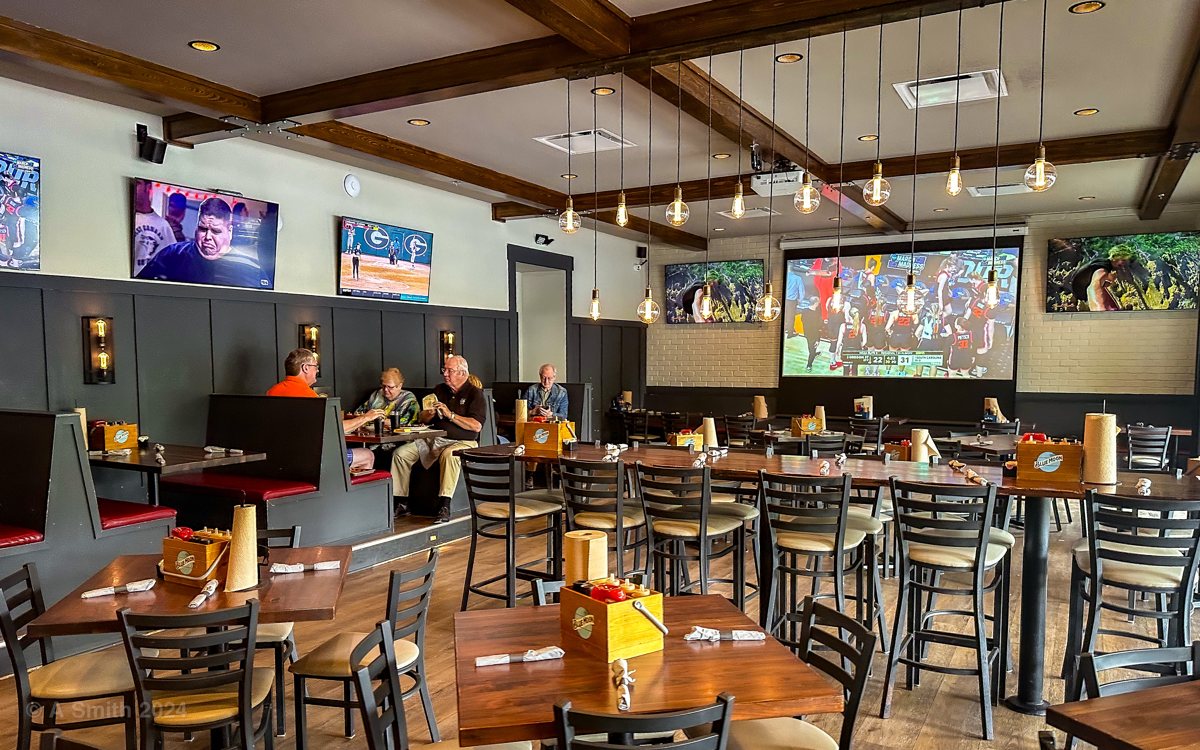 The main dining room at The Smokehouse — booths, high-top tables, pendant lights, and sports screens