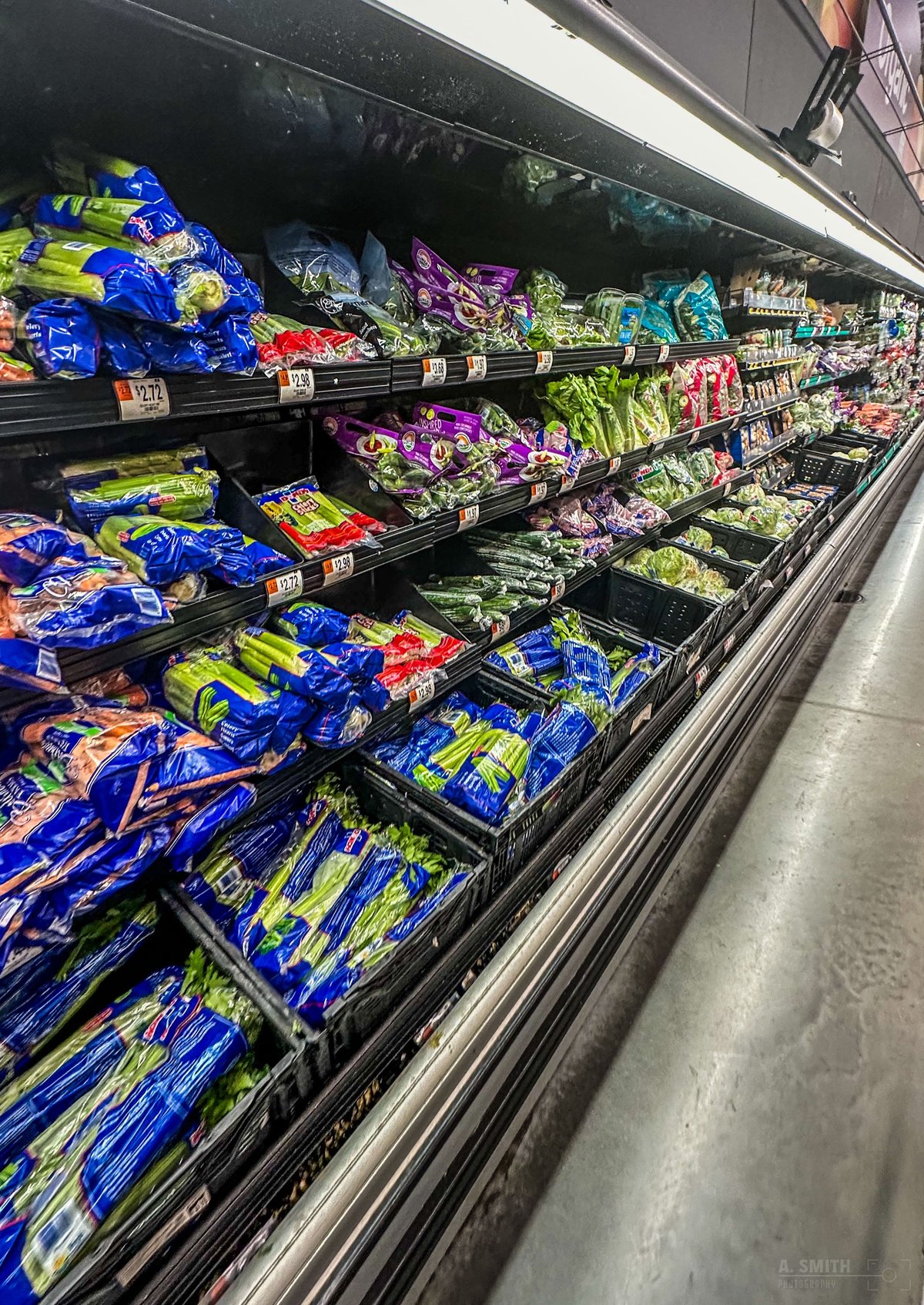 The produce wall inside the Bluffton Walmart — celery and greens in blue bags under the lights