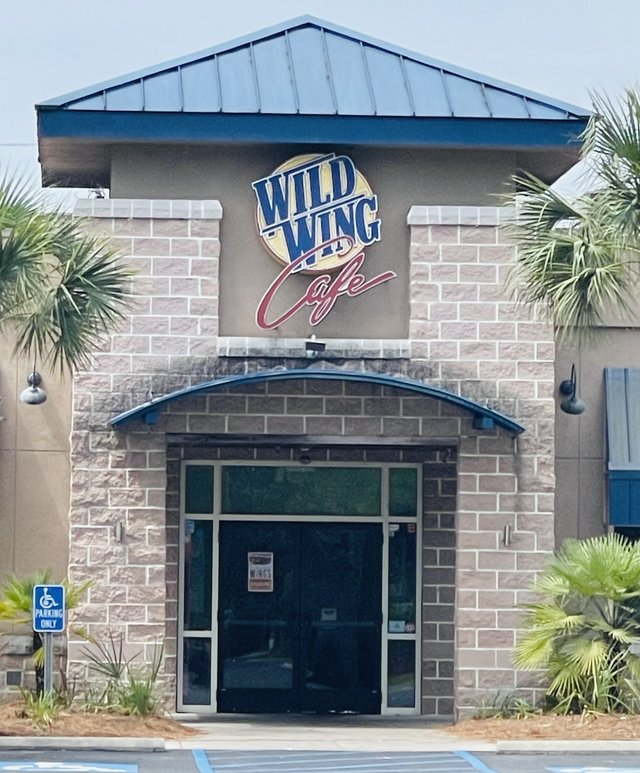 Wild Wing Cafe in Bluffton — stone facade, blue metal roof and the big round WILD WING Cafe sign over the doors